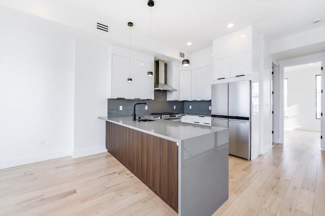 kitchen with stainless steel appliances, a sink, wall chimney range hood, modern cabinets, and a peninsula