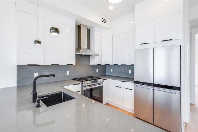 kitchen featuring a sink, white cabinetry, appliances with stainless steel finishes, wall chimney range hood, and modern cabinets