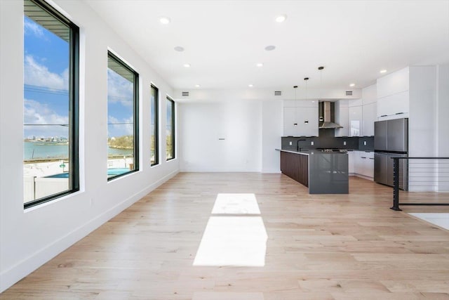 kitchen with white cabinets, wall chimney range hood, light wood-type flooring, freestanding refrigerator, and modern cabinets