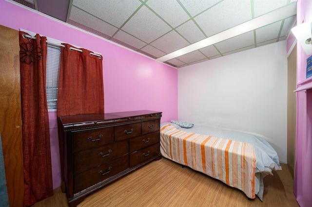 bedroom with a drop ceiling and light wood-type flooring