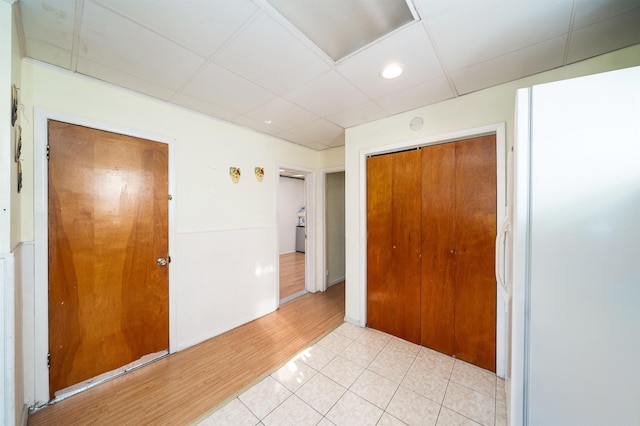 unfurnished bedroom featuring light tile patterned floors, a paneled ceiling, a closet, and white fridge