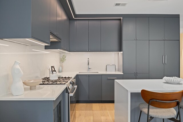 kitchen with gas range, gray cabinets, a kitchen island, and light hardwood / wood-style flooring