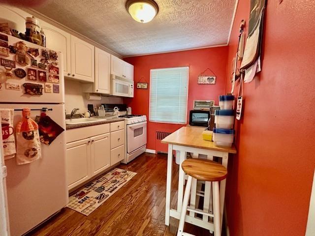 kitchen with dark wood-type flooring, a textured ceiling, white appliances, white cabinetry, and a sink