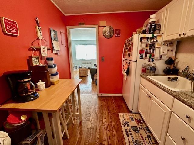 kitchen with a sink, dark wood-style floors, freestanding refrigerator, white cabinets, and baseboards