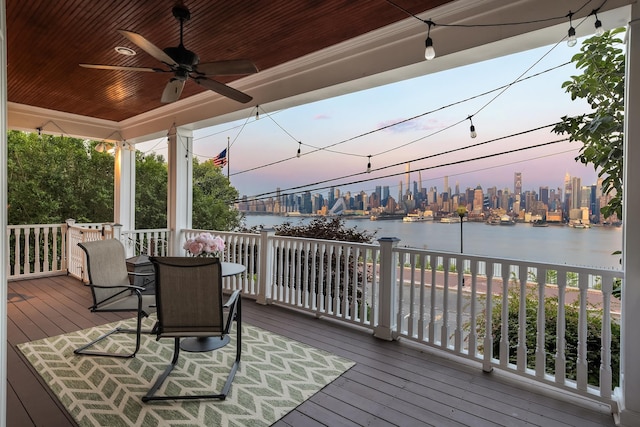 deck at dusk featuring ceiling fan, covered porch, and a water view