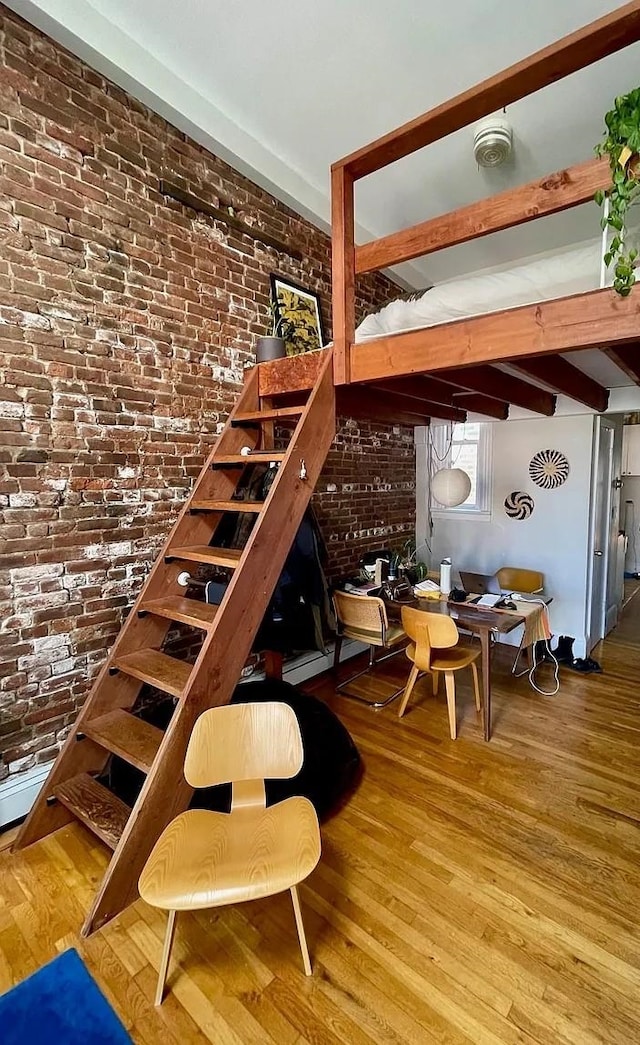 bedroom with wood finished floors and brick wall