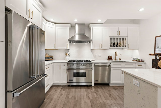 kitchen with white cabinets, wall chimney exhaust hood, light wood-type flooring, high end appliances, and light stone countertops