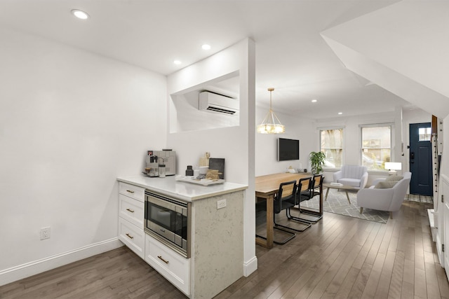 kitchen with hanging light fixtures, dark wood-type flooring, a wall mounted air conditioner, stainless steel microwave, and white cabinets