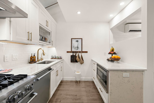 kitchen featuring light stone counters, white cabinetry, appliances with stainless steel finishes, ventilation hood, and sink