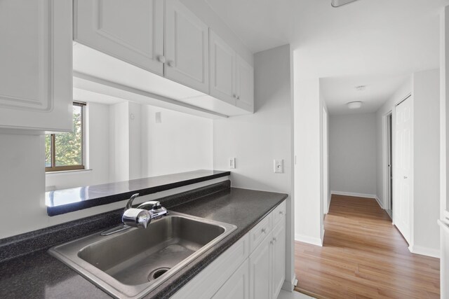 1 2nd St Unit 314, Jersey City, NJ 07302 - kitchen featuring a sink, dark countertops, light wood-style flooring, white cabinetry, and baseboards