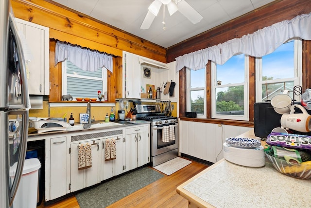 kitchen with stainless steel appliances, a sink, ceiling fan, white cabinetry, and light wood finished floors