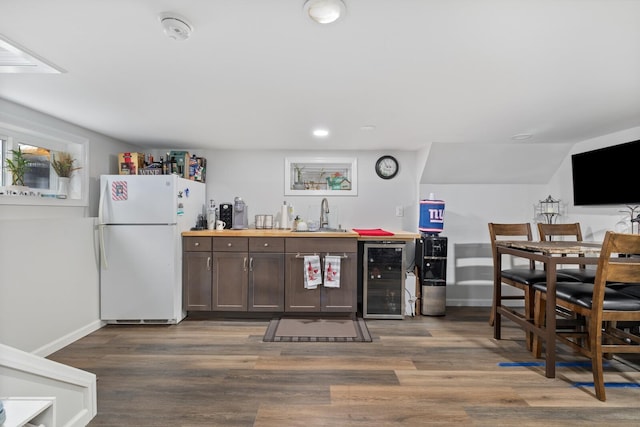 kitchen featuring freestanding refrigerator, beverage cooler, a sink, dark wood-type flooring, and dark brown cabinets