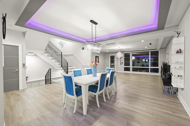 dining space with a chandelier, light wood-type flooring, and a tray ceiling