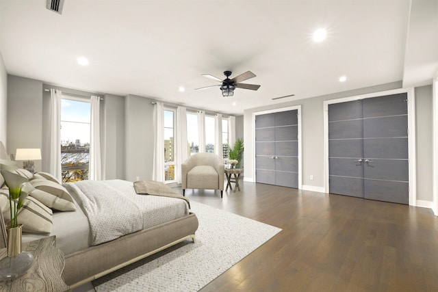 bedroom with dark hardwood / wood-style flooring, two closets, and ceiling fan