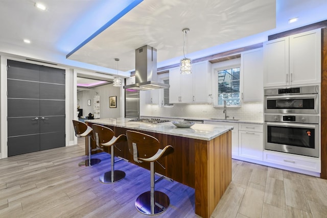 kitchen featuring island exhaust hood, light stone counters, pendant lighting, white cabinets, and a kitchen island