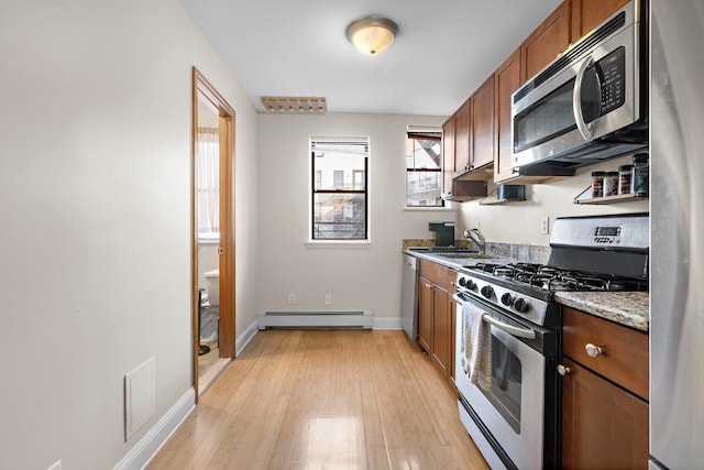 kitchen with light wood finished floors, brown cabinetry, baseboard heating, stainless steel appliances, and a sink