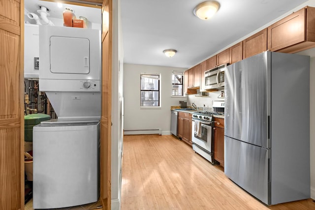 kitchen featuring light wood finished floors, stacked washer / drying machine, a baseboard radiator, appliances with stainless steel finishes, and brown cabinetry