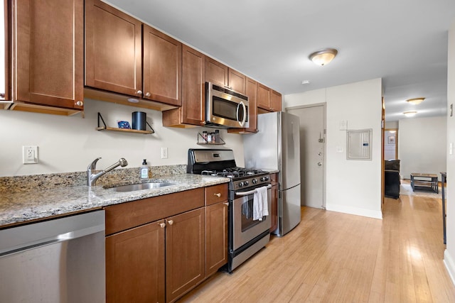 kitchen featuring light stone counters, stainless steel appliances, a sink, baseboards, and light wood-type flooring