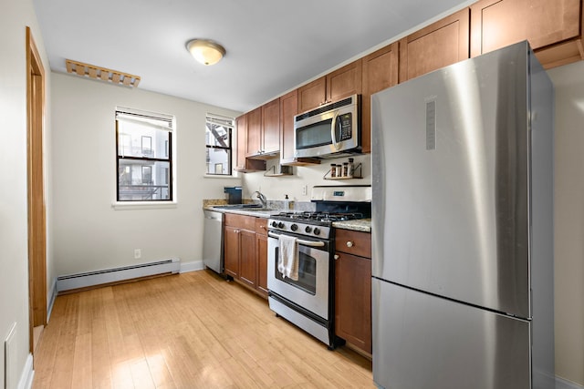 kitchen featuring a sink, light wood-style floors, appliances with stainless steel finishes, baseboard heating, and brown cabinets