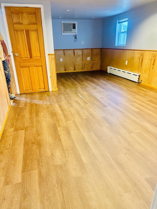 empty room with wood walls, light wood-type flooring, an AC wall unit, and baseboard heating