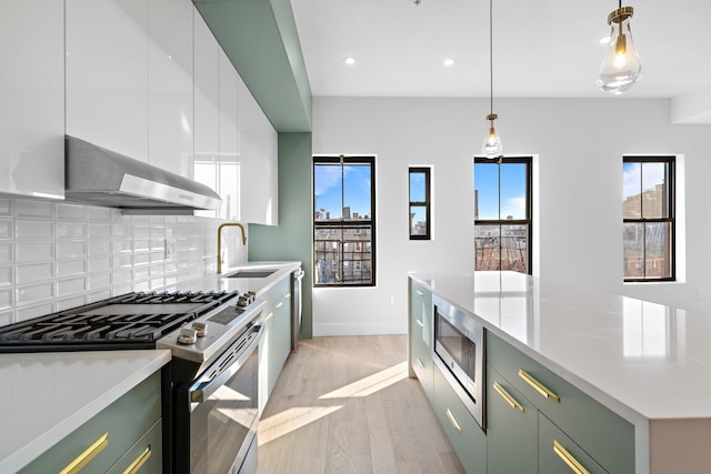 322 3rd St Unit D, Jersey City, NJ 07302 - kitchen with appliances with stainless steel finishes, wall chimney exhaust hood, white cabinets, light wood finished floors, and decorative backsplash
