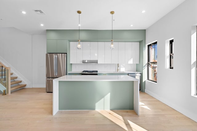 322 3rd St Unit D, Jersey City, NJ 07302 - kitchen with appliances with stainless steel finishes, under cabinet range hood, a center island, backsplash, and light wood finished floors