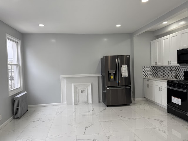 kitchen featuring radiator heating unit, black appliances, white cabinetry, marble finish floor, and backsplash