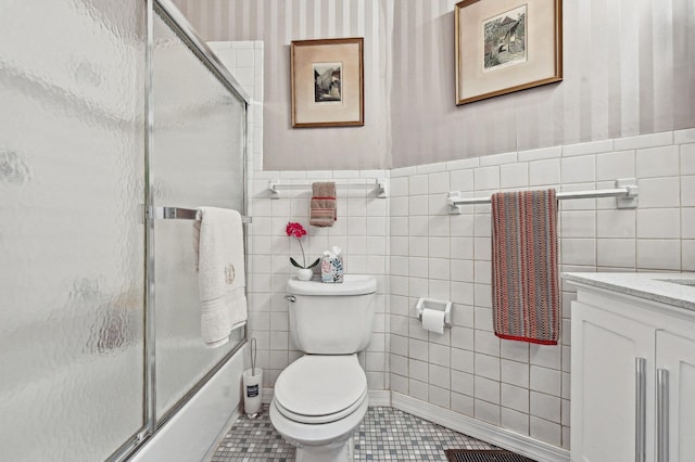 full bathroom featuring combined bath / shower with glass door, tile walls, vanity, tile patterned floors, and toilet