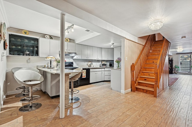 kitchen with white cabinetry, light hardwood / wood-style flooring, a kitchen breakfast bar, black dishwasher, and kitchen peninsula