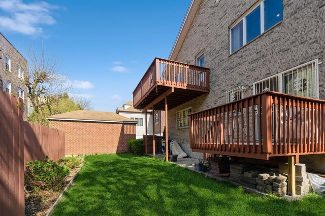 back of house with a lawn, fence, a deck, and brick siding