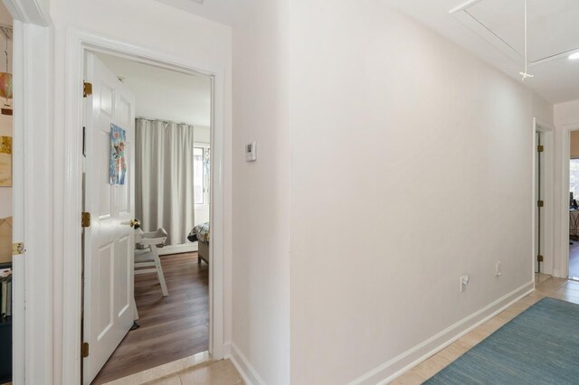 corridor with baseboards, plenty of natural light, attic access, and light wood-style floors