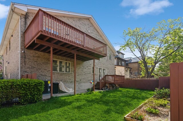 back of property featuring a lawn, a deck, central AC unit, brick siding, and fence