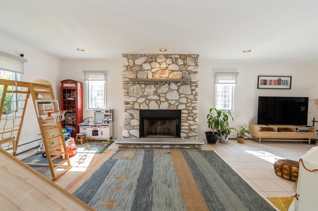 tiled living area featuring arched walkways, plenty of natural light, a baseboard heating unit, and a stone fireplace