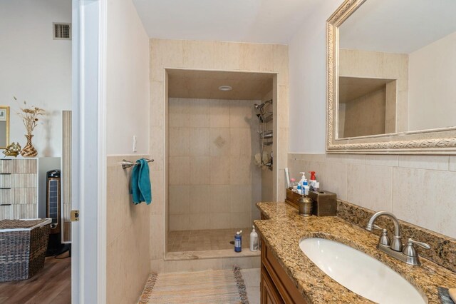 bathroom featuring visible vents, vanity, wainscoting, tile walls, and a walk in shower