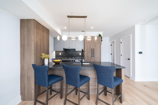 kitchen featuring decorative backsplash, stainless steel gas cooktop, sink, light hardwood / wood-style flooring, and hanging light fixtures