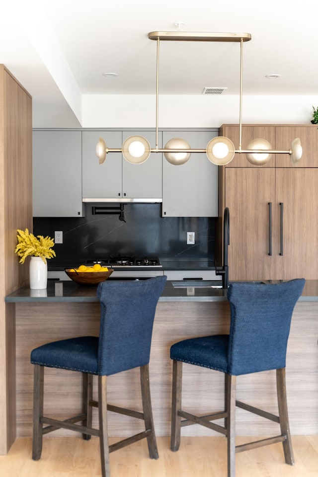 kitchen featuring a kitchen breakfast bar, light hardwood / wood-style floors, black gas stovetop, and tasteful backsplash