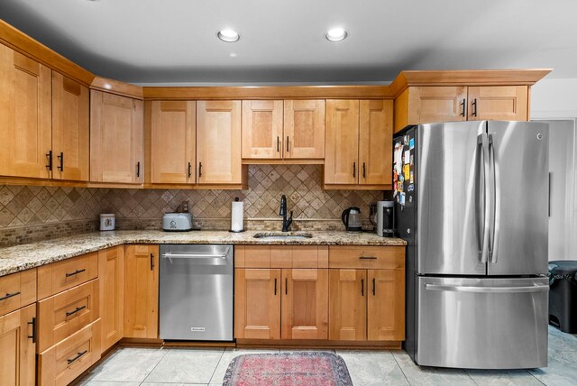 kitchen with backsplash, light stone countertops, appliances with stainless steel finishes, and a sink