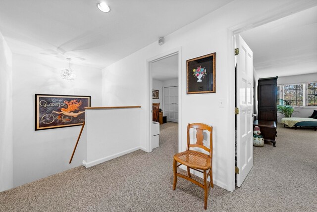 hall with an inviting chandelier, carpet floors, baseboards, and an upstairs landing