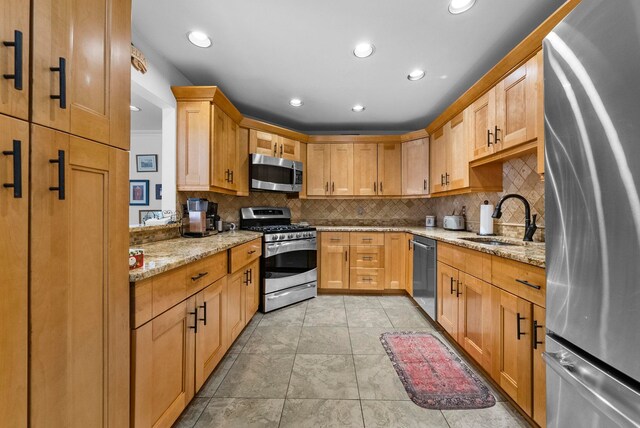 kitchen featuring light stone counters, appliances with stainless steel finishes, a sink, recessed lighting, and tasteful backsplash