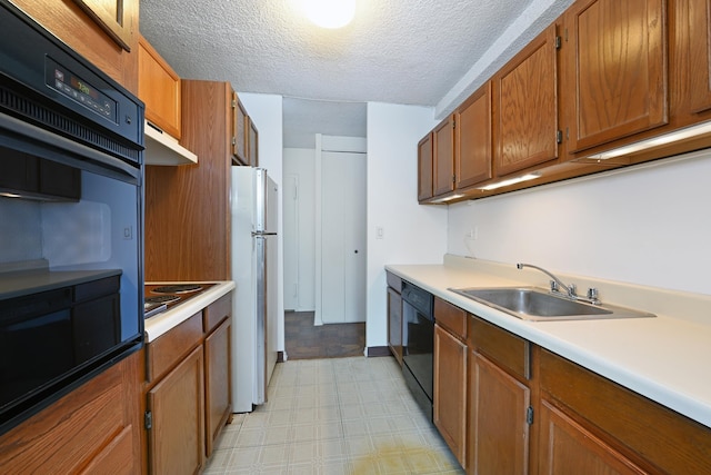 kitchen featuring freestanding refrigerator, under cabinet range hood, dishwasher, brown cabinetry, and a sink