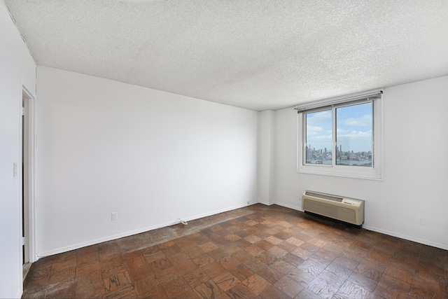 spare room featuring a wall mounted air conditioner, a textured ceiling, and baseboards