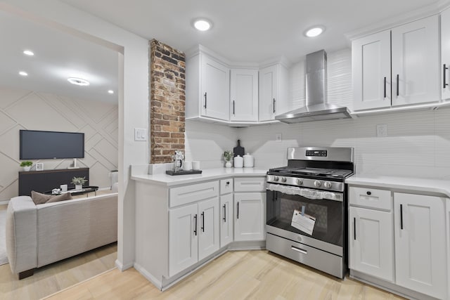 kitchen with white cabinets, stainless steel gas range, wall chimney exhaust hood, and light countertops