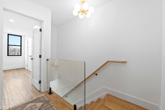 stairway with baseboards, wood finished floors, and an inviting chandelier