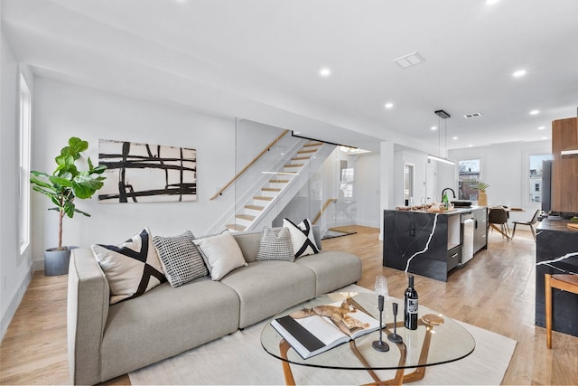 living area with light wood-style flooring, recessed lighting, visible vents, baseboards, and stairway