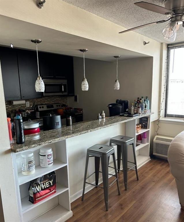 kitchen featuring light stone counters, stainless steel appliances, hanging light fixtures, dark wood-type flooring, and dark cabinets