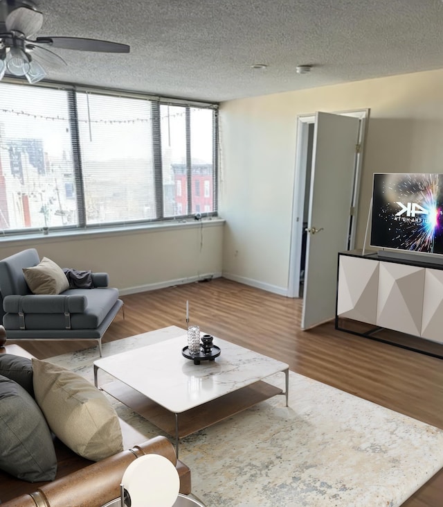 living area with a ceiling fan, a textured ceiling, baseboards, and wood finished floors