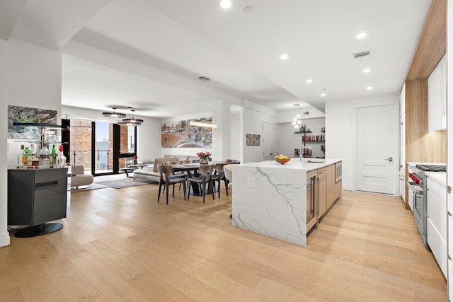 720 Clinton St Unit 6-03, Hoboken, NJ 07030 - kitchen featuring light wood-style floors, a kitchen island with sink, open floor plan, light stone countertops, and decorative light fixtures