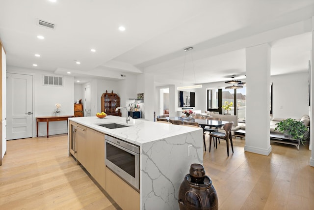 720 Clinton St Unit 6-03, Hoboken, NJ 07030 - kitchen with stainless steel microwave, open floor plan, an island with sink, light wood-style flooring, and light stone counters
