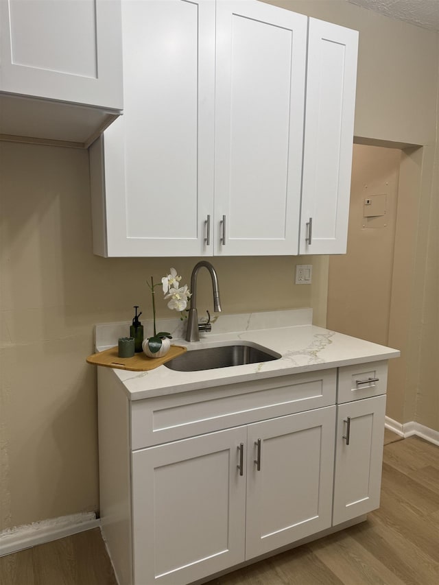 kitchen with a sink, baseboards, light wood-style floors, white cabinetry, and light stone countertops