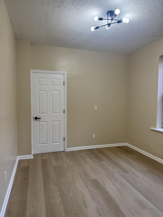 empty room with wood finished floors, a textured ceiling, a chandelier, and baseboards
